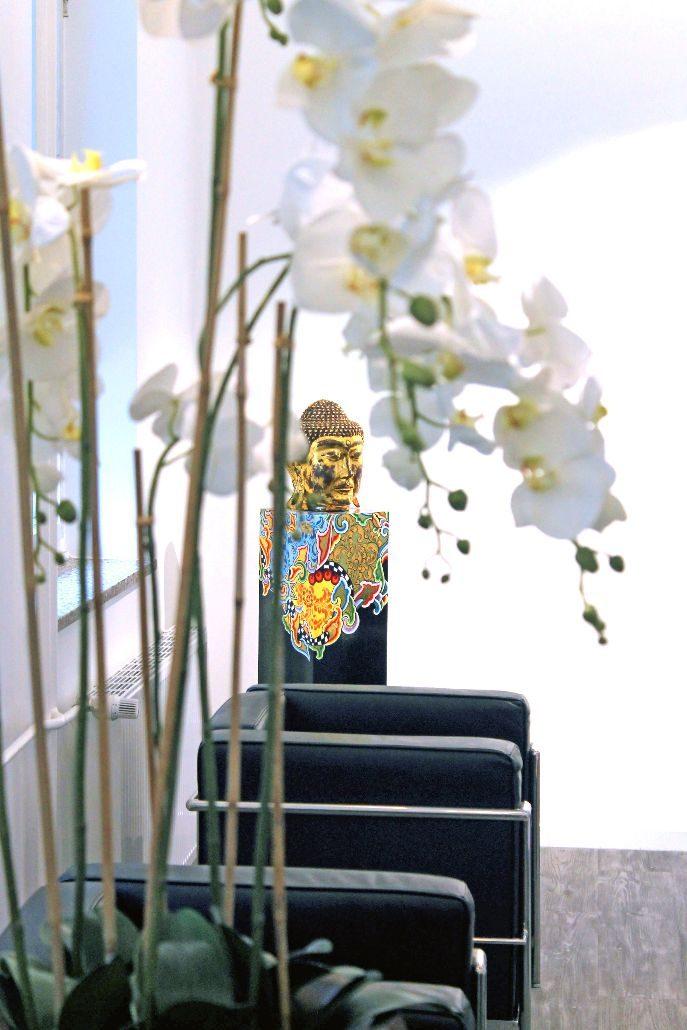 Wartebereich der Praxis mit Sitzgruppe, Orchideen und Buddha-Figur