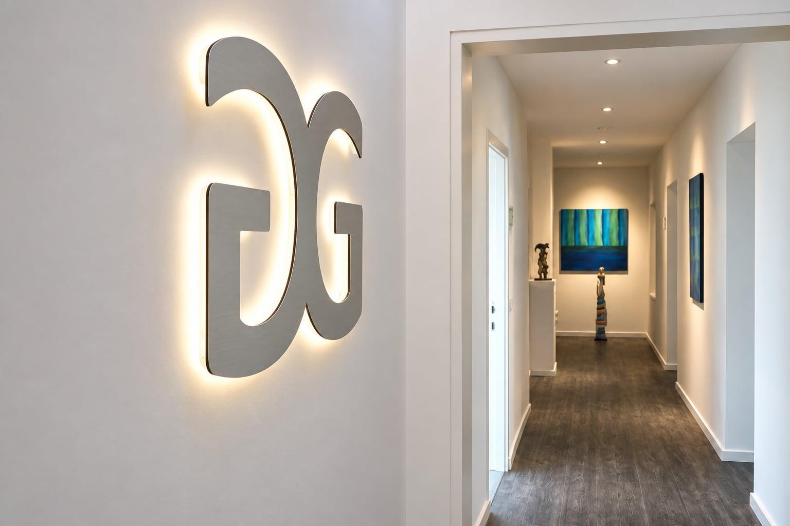 Beleuchtetes Groß-&-Groß-Logo an der Wand, dahinter der Flur mit Bildern