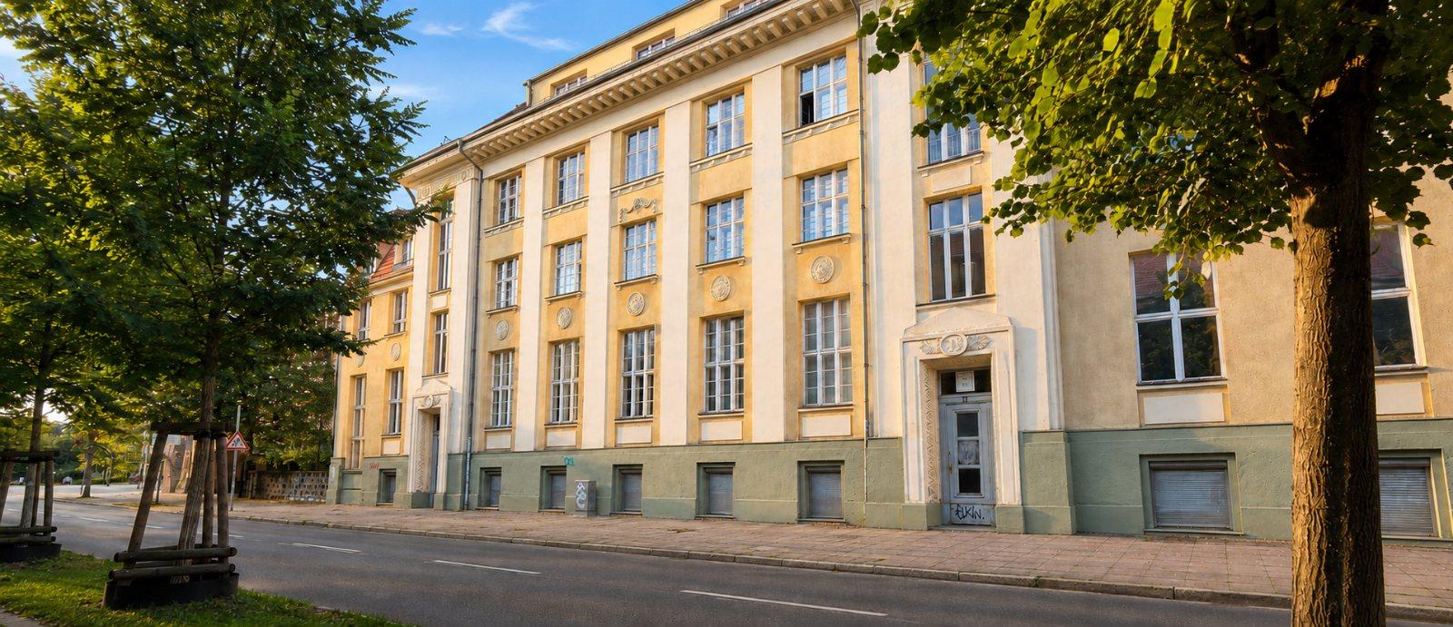Gebäudeansicht von der Schopenhauerstraße: gelbe Fassade mit hohen Sprossenfenstern und Straßenbäumen